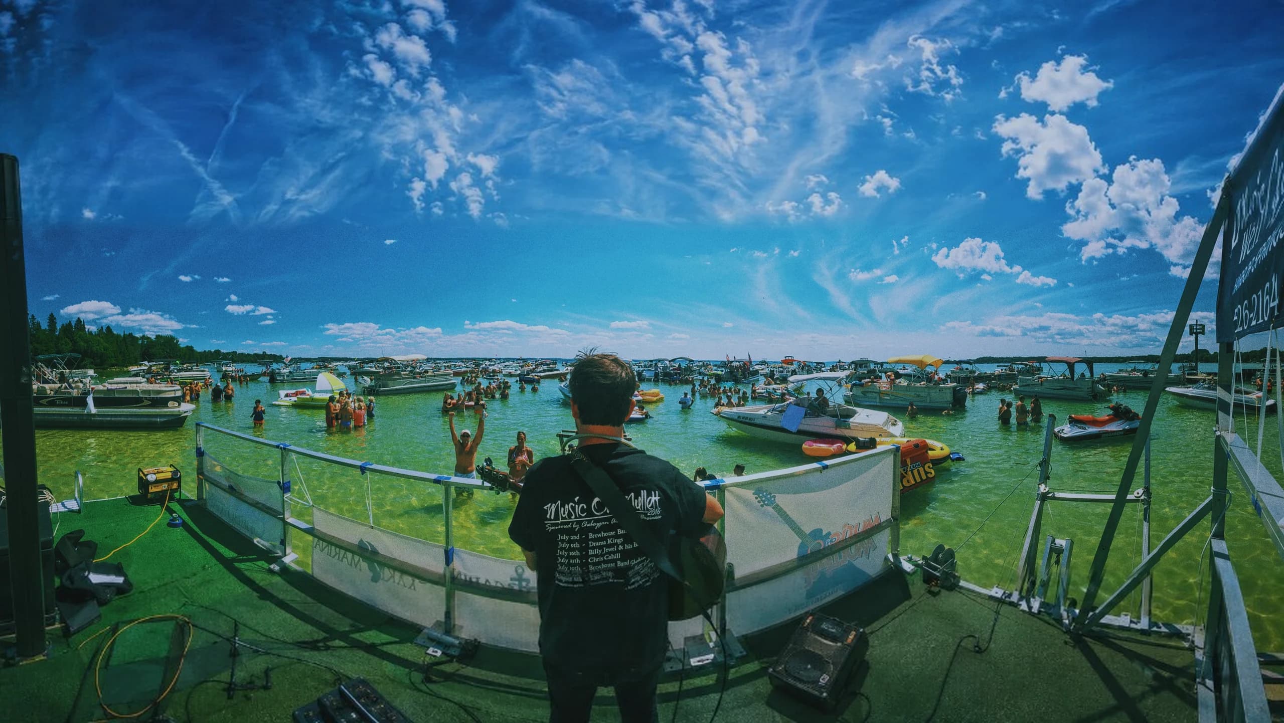 Chris Cahill playing to a sandbar packed with boats at the Music on Mullett series, photographed from behind the stage.