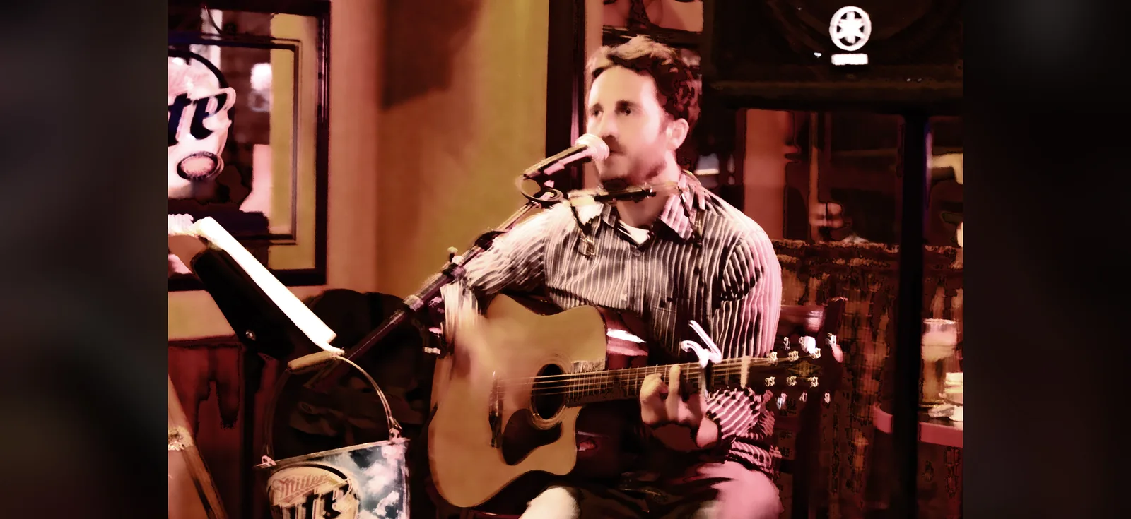 Chris Cahill playing guitar in a dim, warm-lit bar.