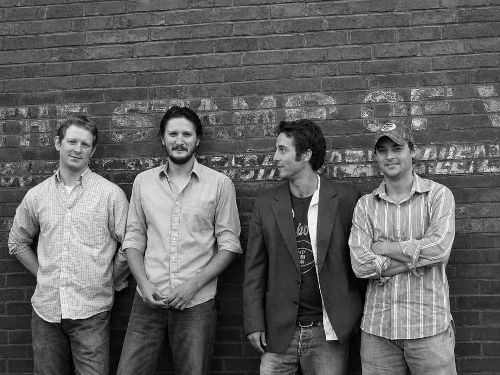 The four members of Cahill & Company against a brick wall, in black and white.