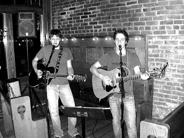 Two members of the band playing a small stage, in black and white.